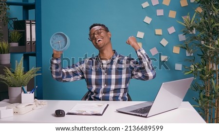 Positive adult holding clock and celebrating time passing, feeling happy about finished work before break. Young man looking at watch with hour and minutes, feeling excited about alarm. Royalty-Free Stock Photo #2136689599