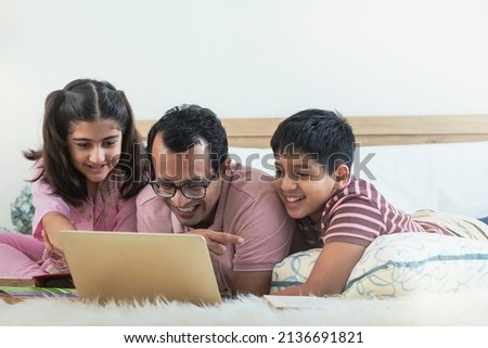 Happy Indian families enjoy surfing the web using laptops computer together on bed at home, Indian family relationship