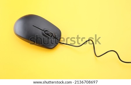 Black mouse with a cord on a yellow background. Empty place for text.