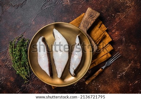 Sliced halibut fish, raw steaks on plate with thyme. Dark background. Top view.