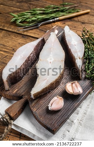 Atlantic halibut fish, raw steaks on wooden board with herbs. Wooden background. Top view.