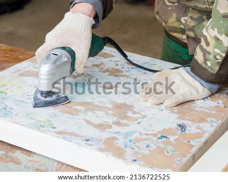 a man using a grinder removes old paint from furniture, restoration of antique furniture. handmade concept Royalty-Free Stock Photo #2136722525