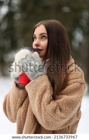 Young woman in cosy fur coat walking in winter forest. Portrait of casual style dressed girl