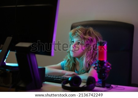 Little kid using desktop pc by night, child boy illuminated by the blue light of a computer screen. Gamer play desktop computer game. Little hacker, young programmer.