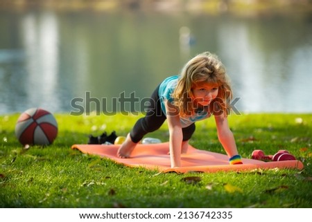 Child is pushing up on the green meadow, working out wearing sportswear, t-shirt outdoor. Kids doing push up outdoor. Gymnastic for children. Kid pushing up. Royalty-Free Stock Photo #2136742335