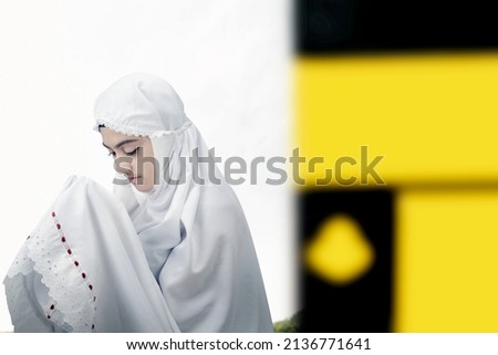 Asian Muslim woman in a veil standing and praying in front of Kaaba with blue sky background