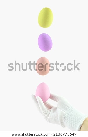 A human hand in a glove tosses up colorful Easter eggs. Easter egg levitation. Creative Easter photo.