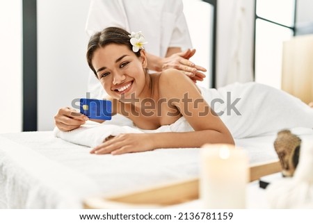 Young latin woman relaxed having back massage holding credit card at beauty center