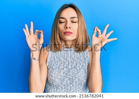 Young caucasian blonde woman wearing casual t shirt relax and smiling with eyes closed doing meditation gesture with fingers. yoga concept. 