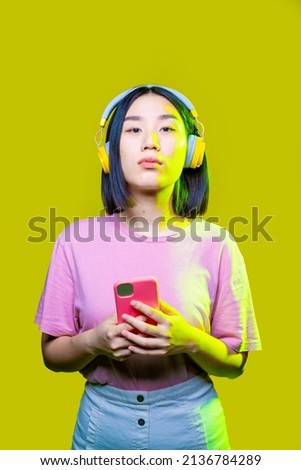Young asiatic woman indoors isolated holding smartphone wearing wireless headphones surfing web 