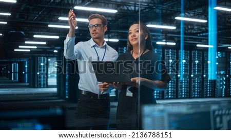 Diverse Big Data Center Server: Entrepreneur and IT Specialist Look at Laptop Screen and Talk. Information Technology Engineer and System Administrator Monitoring Web Services Cloud Solution Software Royalty-Free Stock Photo #2136788151