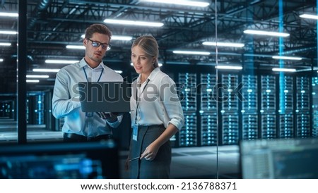Female Chief Engineer Talks with Electronics Specialist, Explaining Things, While Works on Laptop Computer and Agrees with Her. Modern and Evening Office with Stylish Colleagues Royalty-Free Stock Photo #2136788371