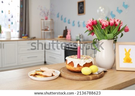 Easter cake, candle, eggs, cookies, picture and vase with tulips on counter in kitchen