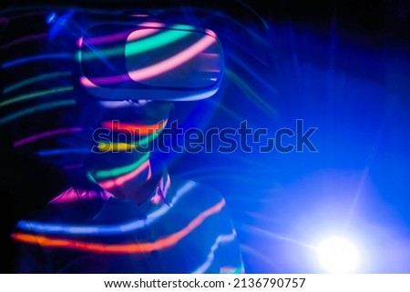 Woman using virtual reality headset, looking around at interactive technology exhibition with multicolor projector light illumination. VR, augmented reality, immersive, entertainment concept Royalty-Free Stock Photo #2136790757