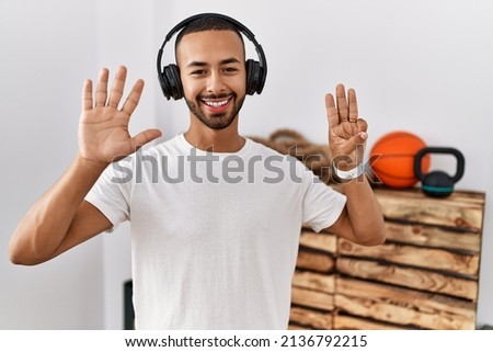 African american man listening to music using headphones at the gym showing and pointing up with fingers number eight while smiling confident and happy. 