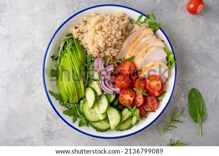 Healthy bowl lunch with grilled chicken, quinoa, avocado, tomatoes, cucumbers and fresh arugula on gray background. Top view. Selective focus