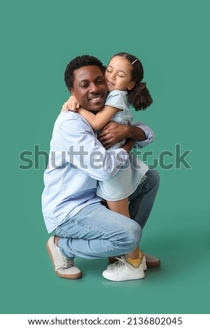 Portrait of little African-American girl hugging her father on green background
