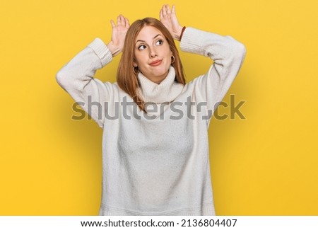 Young irish woman wearing casual winter sweater doing bunny ears gesture with hands palms looking cynical and skeptical. easter rabbit concept. 