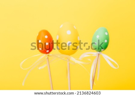 Colorful Easter eggs on sticks on yellow background. Festive Easter holiday greeting card with copy space