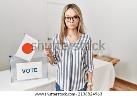 Asian young woman at political campaign election holding japan flag thinking attitude and sober expression looking self confident 
