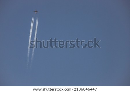 A plane crossing the left of the picture wiew from below, jet in high altitude in blue sky. Airplane with white condensation tracks. Jet plane on clear blue sky with vapor trail