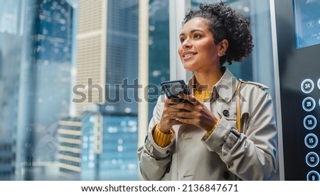 Successful Latin American Female Riding Glass Elevator to Office in Modern Business Center. Beautiful Manager Smile while Using Smartphone, Write Text Message, Check Social Media and Emails in a Lift.