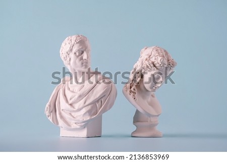 Two small white antique style Roman or Grecian busts depicting men over a blue background Royalty-Free Stock Photo #2136853969