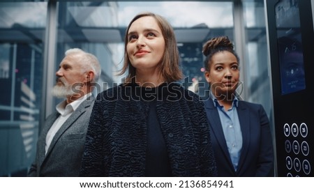 Three Diverse Multiethnic International People Ride a Glass Elevator to Office in a Modern Business Center. Focus on a Happy Young Beautiful Businesswoman Standing in Front in a Lift. Royalty-Free Stock Photo #2136854941