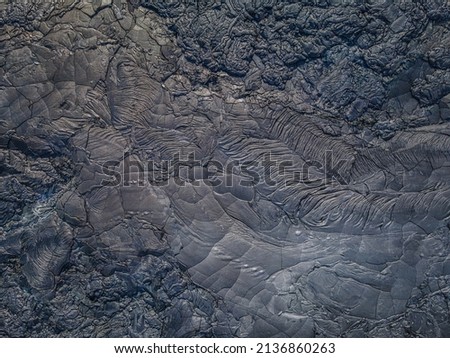 Top view of solidified lava. Dark colored structures from lava flow. Pattern of deferred and broken stones. Different shades of gray. wavy and jagged rigid lava field Royalty-Free Stock Photo #2136860263