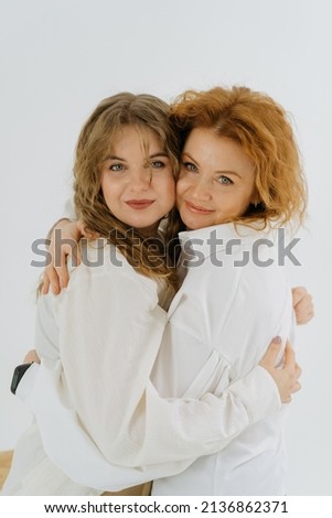 Close-up smiling young woman and her mother hugging, beautiful mom and adult daughter enjoy tender moment, hugging, holding hands, happy family spending leisure time at home together. white. 