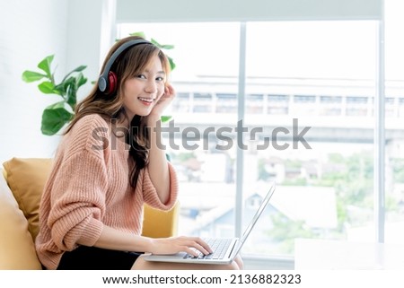 Portrait images of Asian woman, attractive and young,  Sitting on the sofa, wearing earphone and  work from home Which use notebook computers, to work from home and business online concept