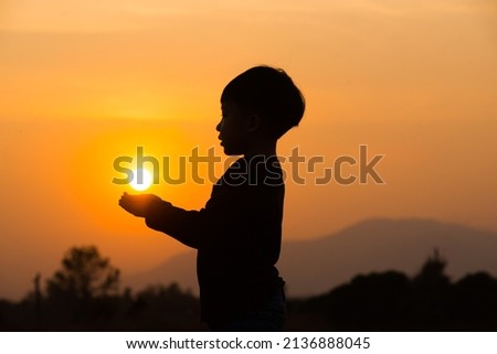 A boy playing with the sun at sun set. Silhouette picture with orange sun set sky. 