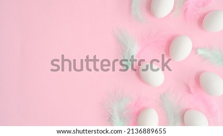 Romantic pastel pink background with white natural eggs and bright feathers. Creative copy space flat lay. Easter composition