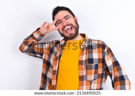 young caucasian man wearing plaid shirt over white background making v-sign near eyes. Leisure, coquettish, celebration, and flirt concept.