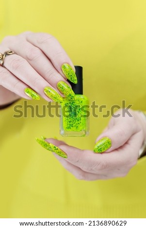 Female hand with long nails and a bottle of bright yellow green neon nail polish