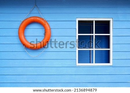 orange life saver ring on blue wooden wall with the window frame