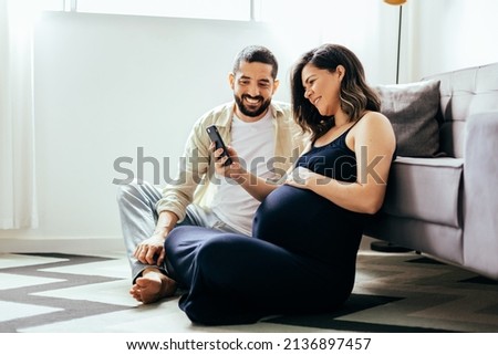 Pregnancy and technology concept. Pregnant woman and her husband spending time together using smartphone. Royalty-Free Stock Photo #2136897457