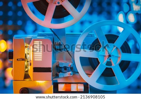 Retro reel with film rotating on sequins kinetic wall, colorful light. Old-fashioned 8mm projector playing in decorated room. Vintage movie objects, cinema, Hollywood concept