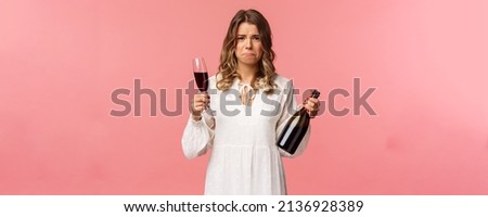 Holidays, spring and party concept. Portrait of upset and whining young blond woman being cheated trying to ease pain with alcohol, holding glass wine and bottle, grimacing want cry, complaining Royalty-Free Stock Photo #2136928389