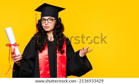 Girl graduate in graduation hat and eyewear with diploma on yellow backdrop. Brunette young woman wearing graduation cap and ceremony robe holding Certificate tied with red ribbon. Education Concept Royalty-Free Stock Photo #2136933429