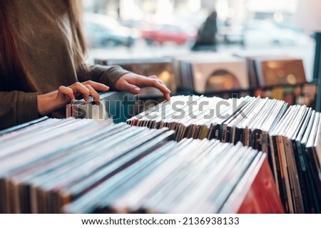 Close up of a woman hands choosing vinyl record in music record shop. Music addict concept. Old school classic concept. Focus on the hands and a vinyl record. Royalty-Free Stock Photo #2136938133