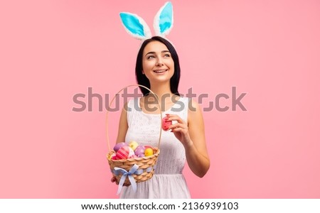 beautiful woman in rabbit ears with a basket of Easter eggs, on the Easter holiday, in a white dress on a pink background. Easter. Resurrection of Christ. High quality photo. High quality photo