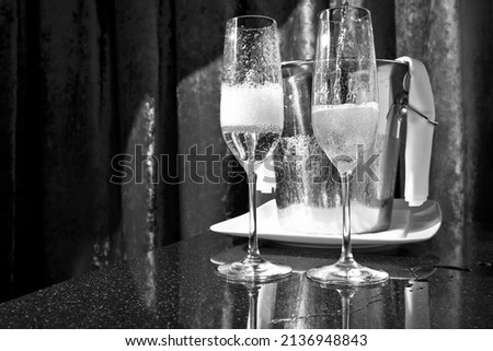 Glasses of champagne on a black table against a pink red curtain. Representing a celebration like a wedding, birthday, Christmas or New Year's Eve. No people, horizontal black and  white image. 