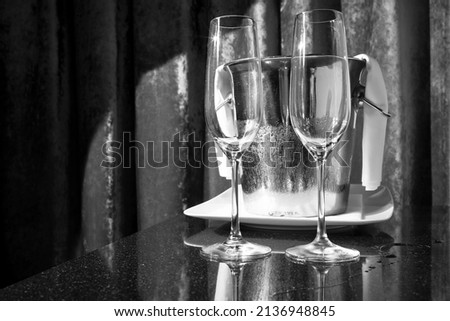 Empty glasses of champagne on a black table against a pink red curtain. Representing a celebration like a wedding, birthday, Christmas or New Year's Eve. No people, horizontal black and  white image. 