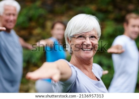 Yoga takes me to my happy place. Shot of a senior woman doing yoga with other people outdoors. Royalty-Free Stock Photo #2136957313