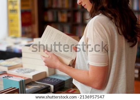 Lost in the pages. A cropped shot of a young woman reading a book while standing in a bookstore. Royalty-Free Stock Photo #2136957547