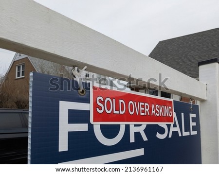 Fresh new sign sold over asking in front of detached house in residential area. Real estate bubble, crash, hot housing market, overpriced property, overpaid, buyer activity concept. Selective focus.