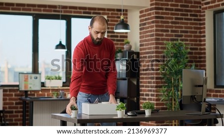 Male entrepreneur getting fired and packing office things to leave job, feeling depressed and shocked about dismissal. Jobless man carrying belongings and thinking about career failure.