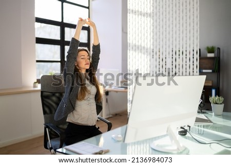 Employee Stretching At Office Desk At Work