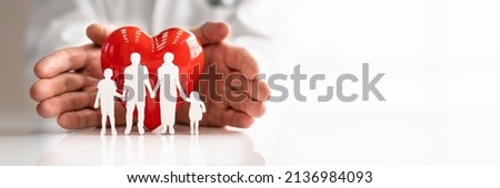 Doctor's Hand Protecting Red Heart With Family Figure On Reflective Desk